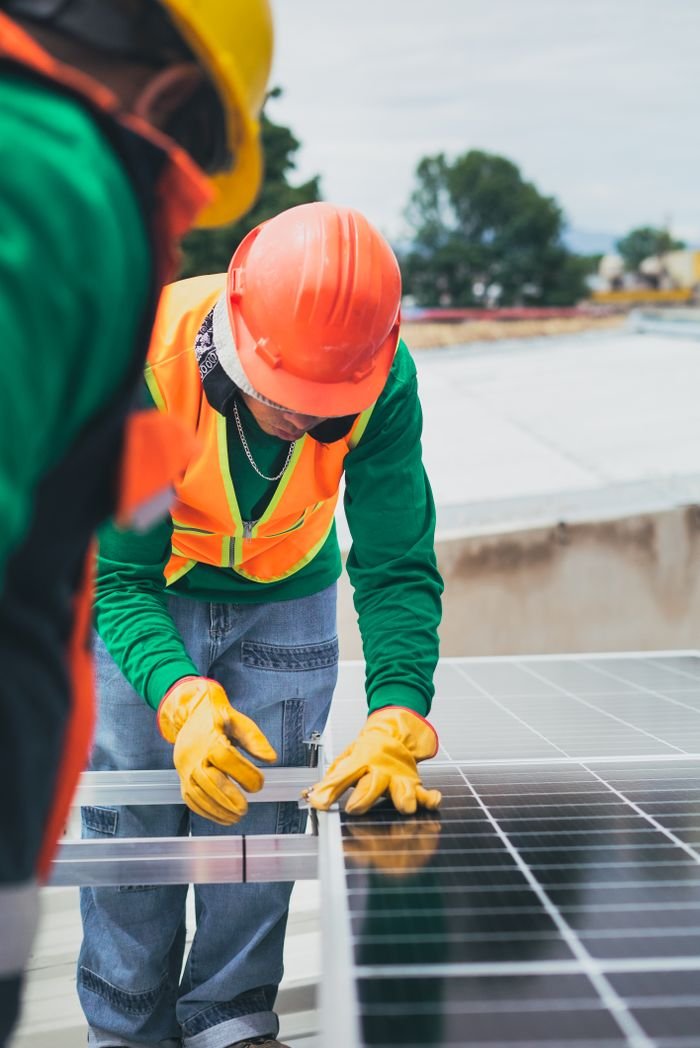 services-03 Worker in safety gear installing solar panels on a rooftop.